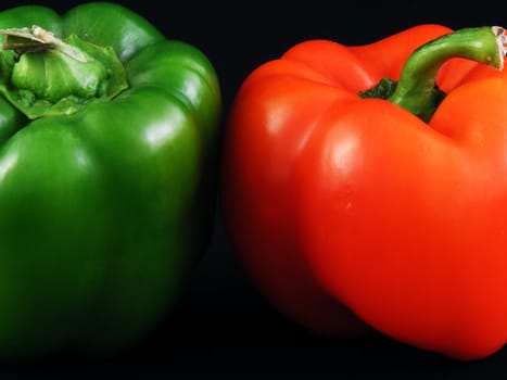 A green and a red bell pepper against a black background.