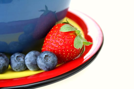 blueberries and a strawberry on a color coordinated plate with a bowl all isolated on a white background