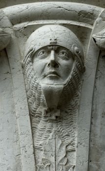 A sculpted soldier's head, protected by a helmet and chain mail, at the top of a pillar on the Doge's Palace in Venice
