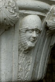 A sculpted soldier's head, protected by a helmet and chain mail, at the top of a pillar on the Doge's Palace in Venice