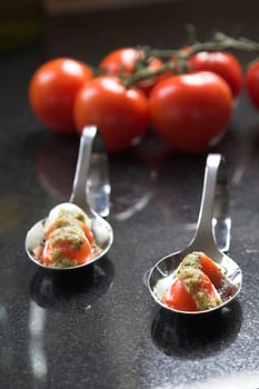Two amuse bouche filled with a small appetizer of cherry tomatoes and mozzarella topped with a sprinkling of green pesto (shallow dof)