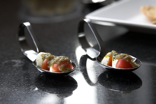 Amuse bouche (small appetizer) filled with cherry tomato, mozzarella and covered with a bit of green pesto