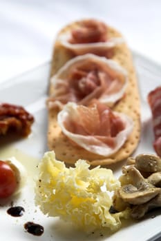 Plate of antipasti with rolled up parmaham on toast, mushrooms, cheese, sprinkled with balsamic vinegar (shallow dof)
