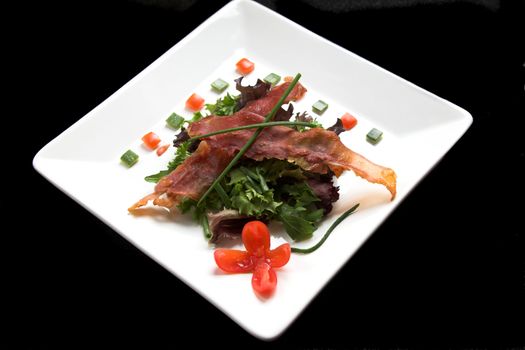 Delicious vegetable salad on a plate decorated with crispy parma ham slices, a flower made out of a tomato and little pepper cubes