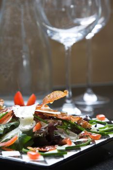 Healthy salad with empty wineglasses and a bottle of water in the background