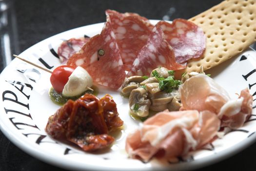 Small plate of antipasti with mushrooms marinated in garlic oil, parmaham, toast, cherry tomato with mozzarella and dried mushrooms