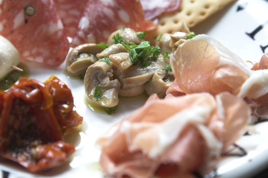 Plate of antipasti with the focus on mushrooms marinated in garlic surrounded by dried tomatoes in oil, chorizo and parma ham 