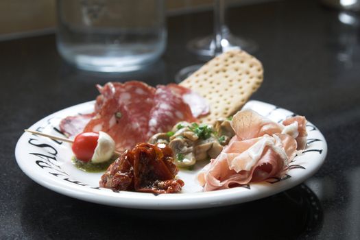 Plate of famous Italian appetizer, antipasti, with dried tomatoes, mushrooms marinated in garlicoil, cherry tomatoes with mozzarella, chorizo and toast