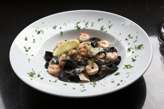 Big plate filled with black pasta with tigerprawns and regular small shrimps; plate is decorated with parsley