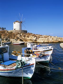 A windmill on the greek island of Mykonos looking down on a small inlet with fishing boats