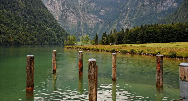 Green water and wooden mooring posts at Koenig See Lake in Bavaria