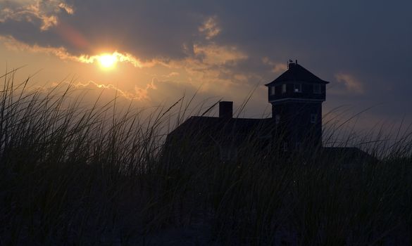 dark dusk sky, grass silhouettes in foreground, lighthouse in background, photo taken on Sandy Hook in New Jersey, USA.