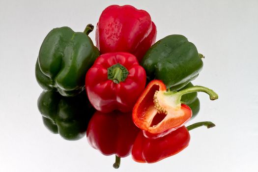 Red and green bell peppers and halved red bell pepper on reflective bacground