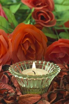 lighted white candle still life scene with red flowers in background