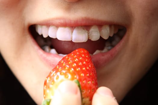 girl puting stawberry to her mouth to eat.
