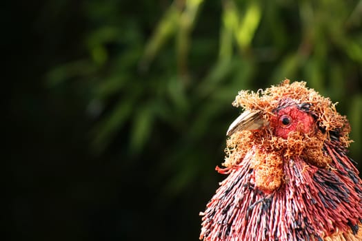 A hand made straw and string constructed chickhen/rooster. A landscape format with soft focus greenery to the background.