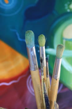 Close up detail of a set of artisist brushes with a soft focus abstract coloured painting in the background, painted by myself as the artist.