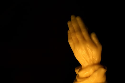A wax candle of hands praying on black.