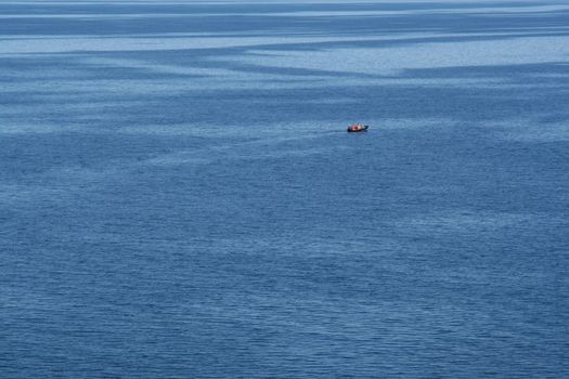 A small boat with a couple occupants in the middle of the open ocean.