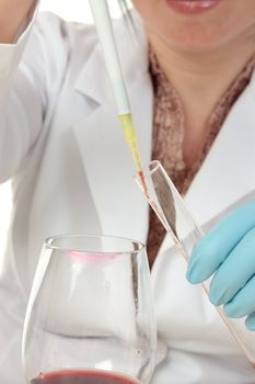 A forensic investigator or criminologist uses a pipette to take a sample of the contents inside a glass for analysis.  Focus to pipette.