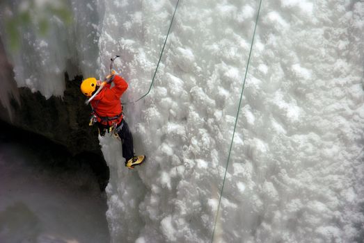 An Ice Climber going up a frozen waterfall.
