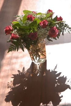 Sunshine on bouquet of red roses and gypsophyla in glass vase