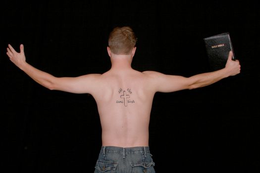 A man preaching with a crucifix and aramiac writing tattooed on his back.
