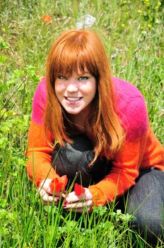 redheaded girl is sitting on a meadow, she has found spring flowers, she is happy