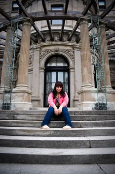 A young latin woman sitting on the steps of an old mansion.
