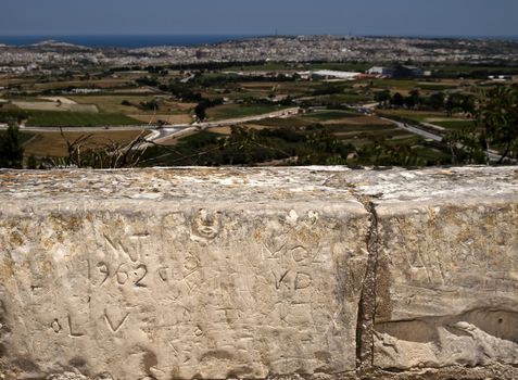Graffiti and inscriptions on a medieval limestone wall with view of Malta in background