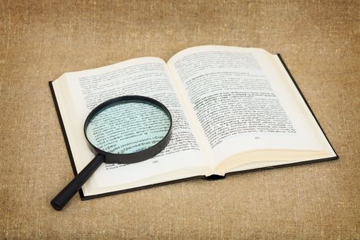 Open book and magnifier on canvas background - a still-life