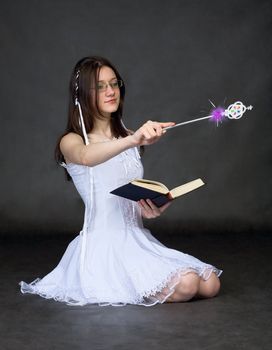 Girl - the sorcerer with the book and a magic wand on black