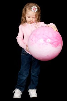 A sad little girl holding her ball, looking down at the ground.