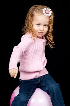 An adorable young child playing on a pink ball.