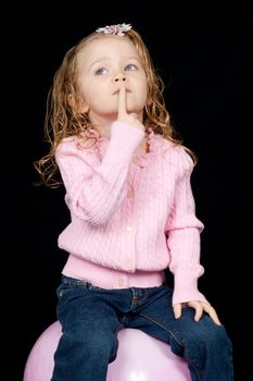 A serious young child sitting on a ball, thinking.