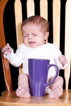 A photograph of a baby sitting on the chair with her coffee cup.  I act like a baby in the morning until I get my coffee!