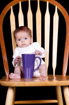 A photograph of a baby sitting on the chair with her coffee cup.  I act like a baby in the morning until I get my coffee!