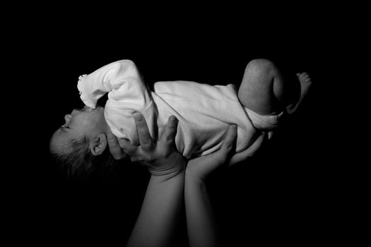 A baby being held in the air.  The child is risen above.  Image in black and white.