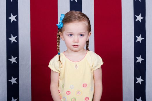 A confused child standing in front of an American Flag style background.