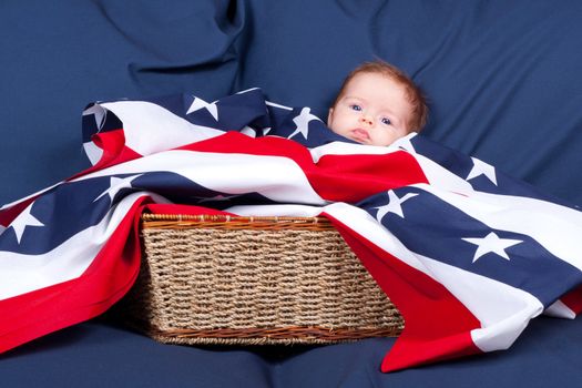 A cute little baby in a straw basket.  The baby is using the flag pattern as a blanket and has a blue background.