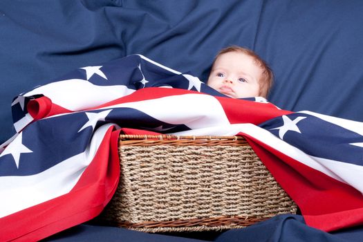 American baby laying in a basket with an american flag covering her.