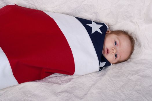 A baby swattled in an american flag fabric/blanket.