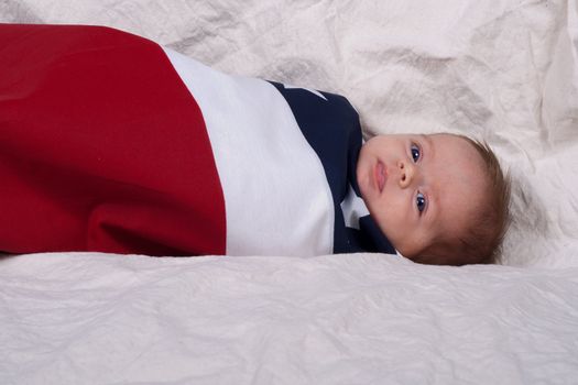 An american baby wrapped in a swattle with red white and blue and some stars on it.