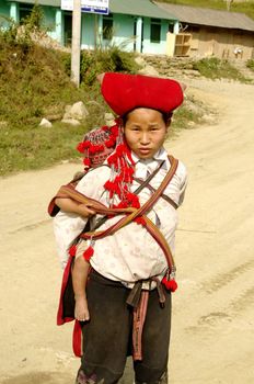 Nearly SAPA, City of North Vietnam. A woman of the ethnic (minority) Hmong Red pompoms with her baby in the back. She wears her beautiful costumes and hairstyle typical. Her baby was also a traditional cap color
