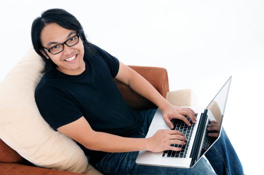 Happy young man sitting on sofa and using laptop.