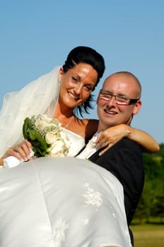 Groom is lifting his bride up in a park.