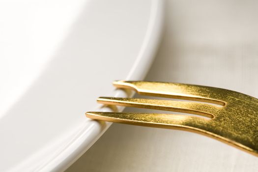 Fragment of kitchen ware - a white plate and a Gold fork on a plate
