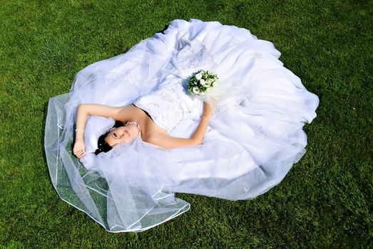 Bride lying on a wedding dress on the grass.