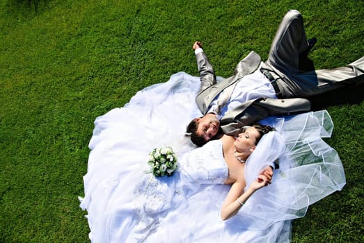 Bride and groom lying on a wedding dress on the grass.