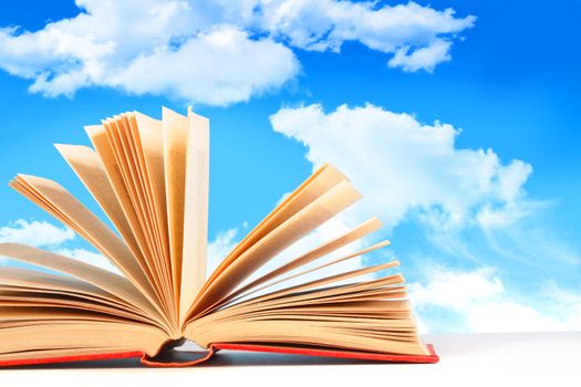 Open book on white surface against a blue sky